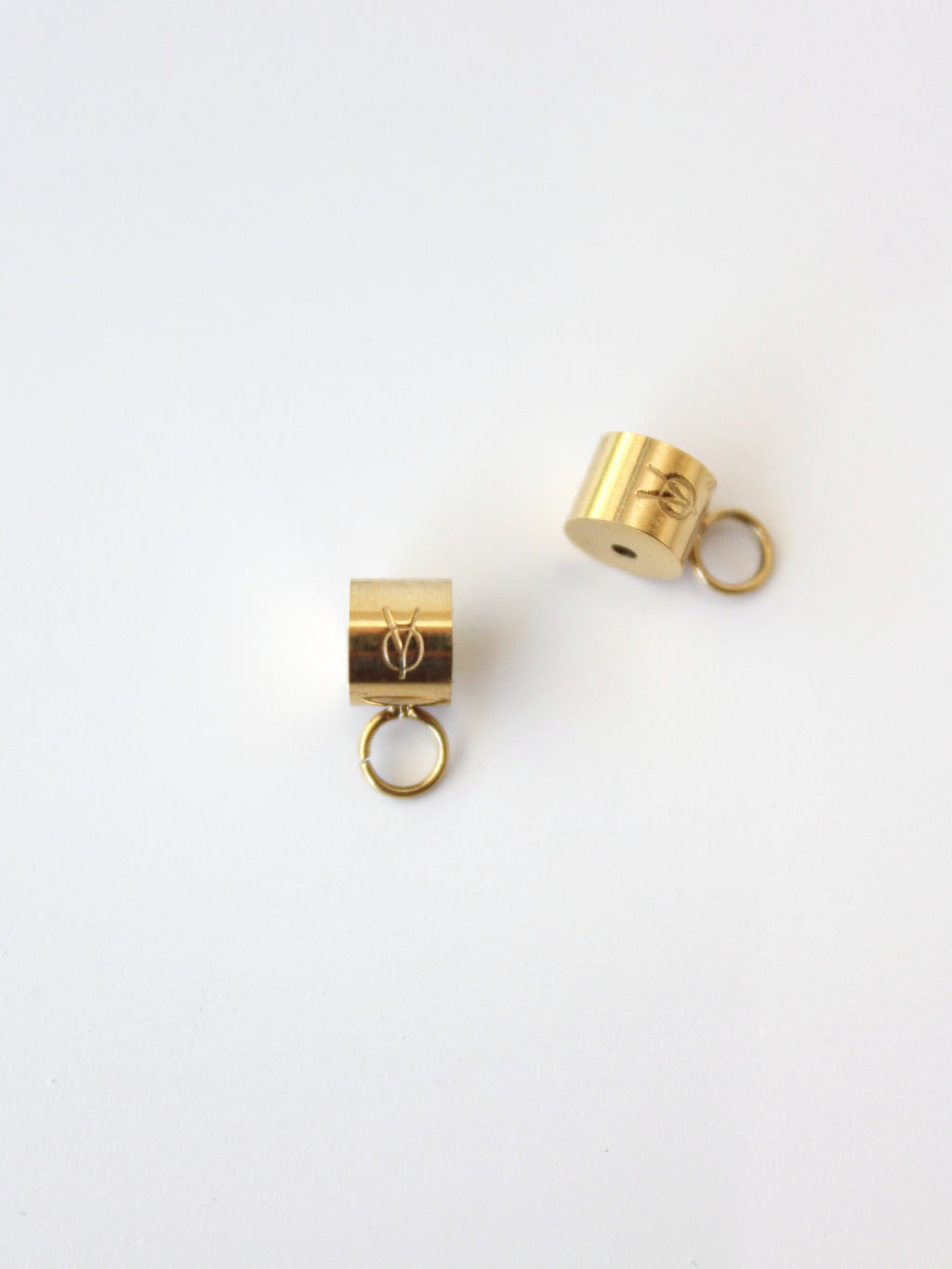 Two gold cylindrical charms with loops on a white background